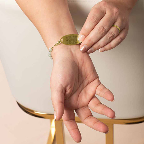 Close-up of a woman’s wrist with her palm facing up, showing the underside of a Leah Mist Gold medical ID bracelet with engraved medical information on a gold tag.