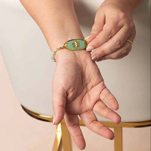 Front view of Leah Mist Gold medical ID bracelet on wrist, highlighting the gold medical tag with aqua inlay and white medical symbol.