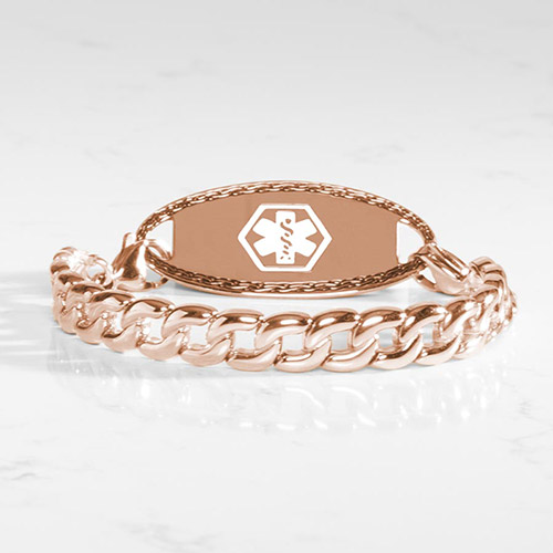 Women's rose gold medical ID bracelet with bold curb chain links and a polished engraving plate featuring the white medical caduceus symbol, styled on a white marble surface.