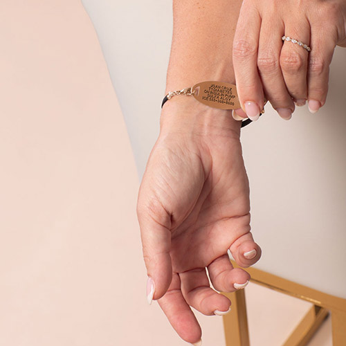 Close-up of gold medical alert bracelet for women with white medical symbol on face, featuring black strap and customizable engraving for health emergencies.