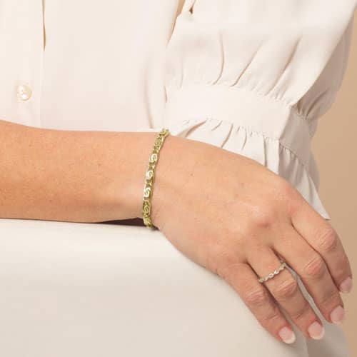 Woman wearing a gold bracelet with decorative swirl links, styled as an elegant medical ID bracelet for everyday safety and style.