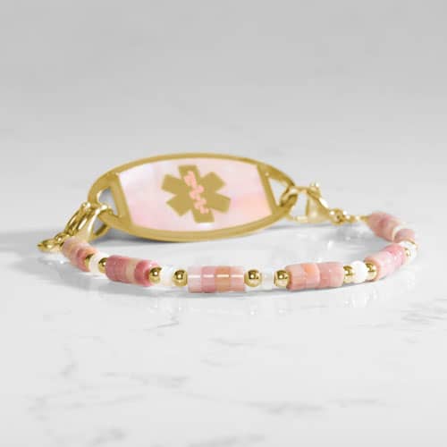 Beaded bracelet featuring gold tone and Heishi beads in cream and rose on a stretch bracelet, attached to a gold tone medical ID with a gold tone medical ID tag with Pink Mother of Pearl id and gold tone caduceus medical symbol. 