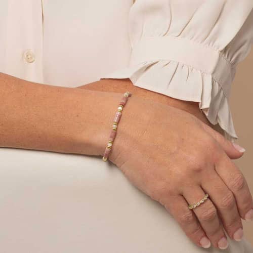 Woman displaying a Beaded bracelet featuring Gold tone and Heishi beads in cream and rose on a stretch bracelet. 