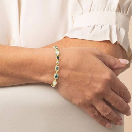 Woman wearing a gold gemstone bracelet with blue and pearl accents, styled as an elegant medical ID bracelet for everyday wear.