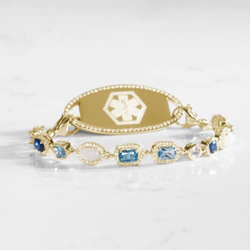 Gold medical ID bracelet with blue gemstone and pearl accents, featuring an engraved medical emblem for elegant everyday safety.