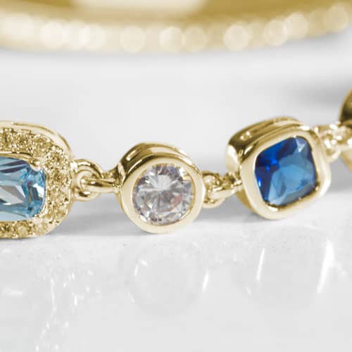 Close-up of blue and clear gemstone bracelet links in gold settings, showcasing elegant detailing on a stylish medical ID bracelet.