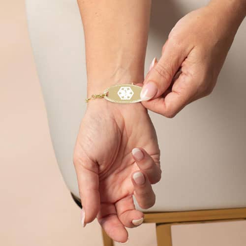 Woman holding a gold medical ID bracelet with engraved medical emblem, combining elegant jewelry style with emergency safety.