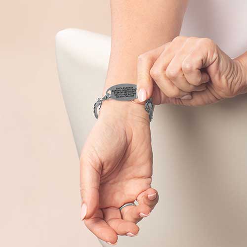 Woman wearing silver medical ID bracelet with engraved emergency information on underside of tag for discreet safety.