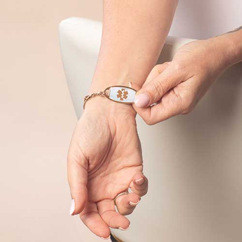 Close-up of woman flipping rose gold medical ID bracelet to reveal front tag with medical alert symbol.