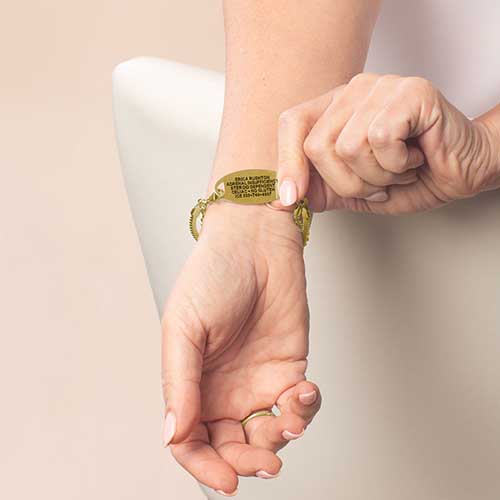 Woman wearing gold medical ID bracelet showing engraved emergency information on underside for discreet identification.