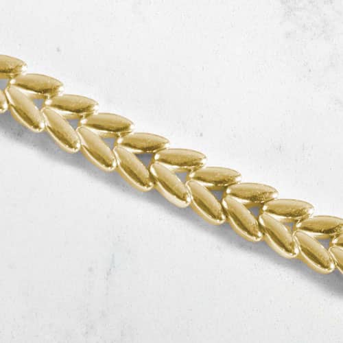 Close-up of polished gold-tone chevron links arranged in a textured, herringbone-inspired pattern.