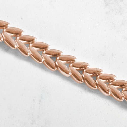Close-up of polished rose gold-tone chevron links arranged in a textured, herringbone-inspired pattern.