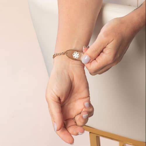 Person revealing the front of a rose gold-tone medical ID bracelet with a white mother-of-pearl inlay and Star of Life symbol.