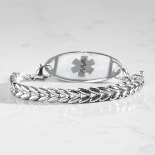 Silver tone chevron link bracelet with oval medical ID tag displayed on a light stone surface.
