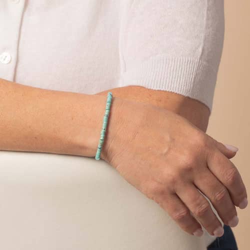 Model wears a silver-tone medical ID bracelet with turquoise heishi beads and a slim, minimalist profile.