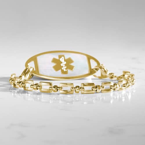 Gold Hadley medical ID bracelet with mother-of-pearl tag photographed on a white marble surface.