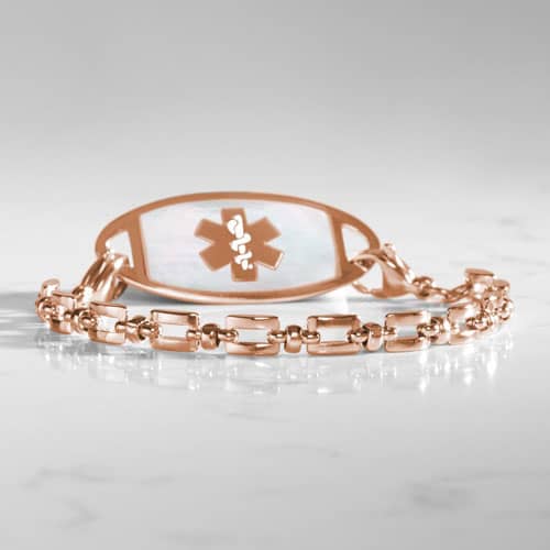 Rose gold Hadley medical ID bracelet with mother-of-pearl tag photographed on a white marble surface.