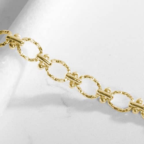 Close-up of the Iris bracelet's textured oval links and bead accents, highlighting the polished gold-tone finish and intricate details.