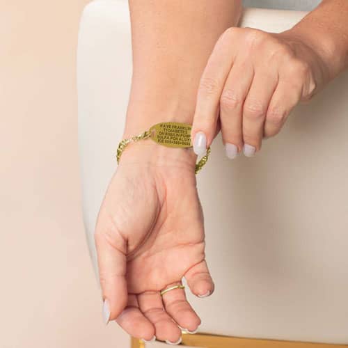 Model lifts the oval medical ID tag to display the engraved medical information on the back of the gold-tone bracelet.