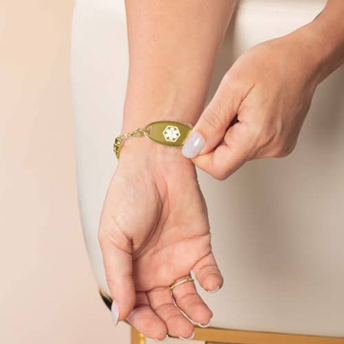 Model lifts the oval medical ID tag to display the white medical symbol on the front of the gold-tone bracelet.