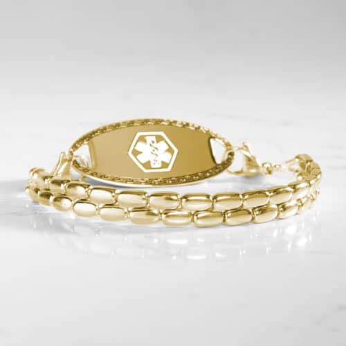 Gold-tone medical ID bracelet with a double-row rectangular link design and oval ID tag displayed on a marble surface.