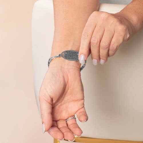Model lifts the oval medical ID tag to display the engraved medical information on the back of the silver-tone bracelet.