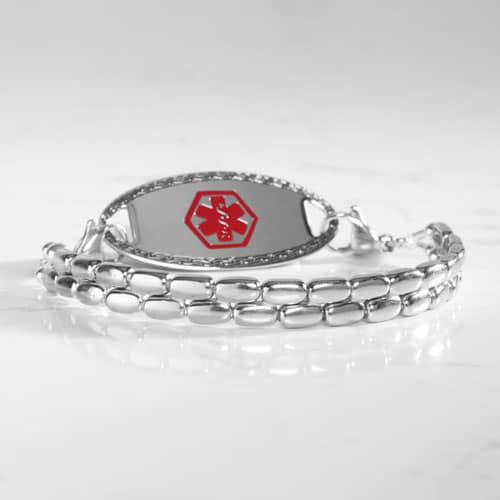 Silver-tone medical ID bracelet with a double-row rectangular link design and oval ID tag displayed on a marble surface.