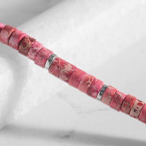 Close-up of pink jasper heishi beads with natural marbled patterns and polished silver spacer accents.