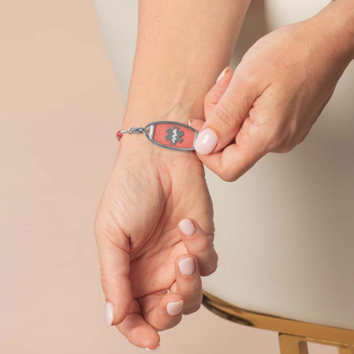 Person revealing the front of a silver-tone medical ID bracelet with a pink stone inlay and Star of Life symbol.