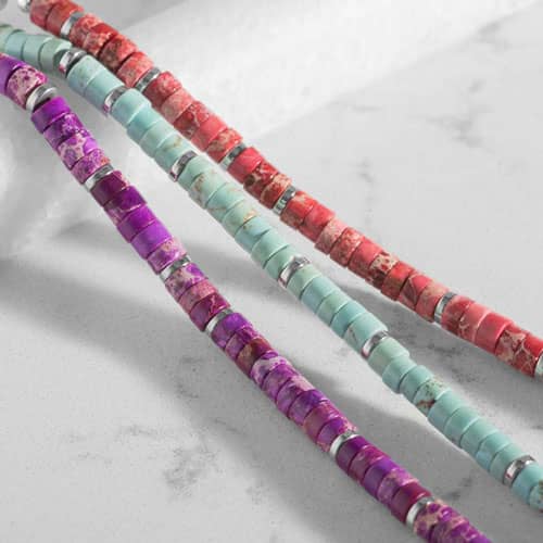 Close-up of purple, turquoise, and coral heishi bead bracelets with silver spacer accents shown side by side.