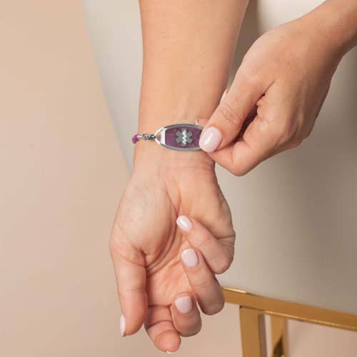 Person revealing the front of a silver-tone medical ID bracelet with purple stone inlay and Star of Life symbol.