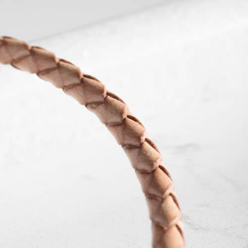 Close-up of the light tan braided bracelet, highlighting its woven texture and natural color variation.