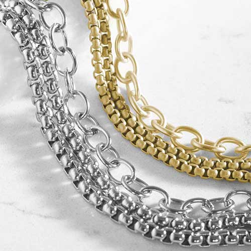 Close-up of silver-tone and gold-tone layered bracelet designs featuring mixed chain textures and oval link accents.