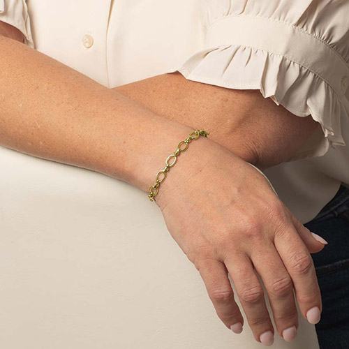 Model wearing a delicate gold-tone oval-link bracelet on her wrist.