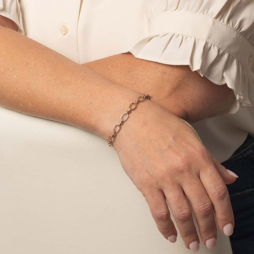Model wearing a delicate rose gold-tone oval-link bracelet on her wrist.