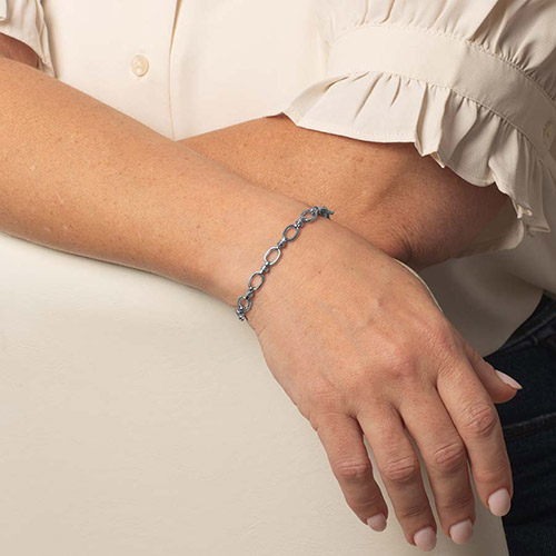 Model wearing a delicate silver-tone oval-link bracelet on her wrist.