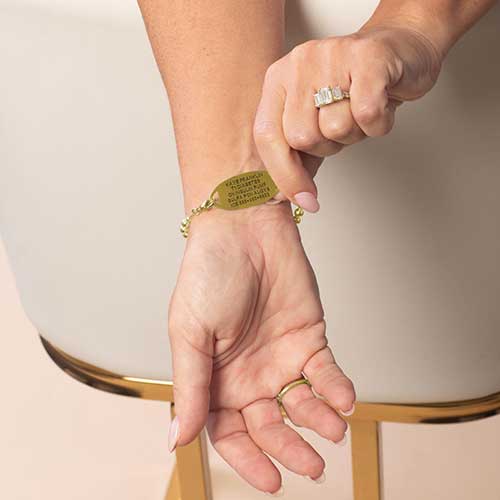 Model is wearing a gold-tone medical ID bracelet, displaying the back of the ID tag with personalized medical engraving.