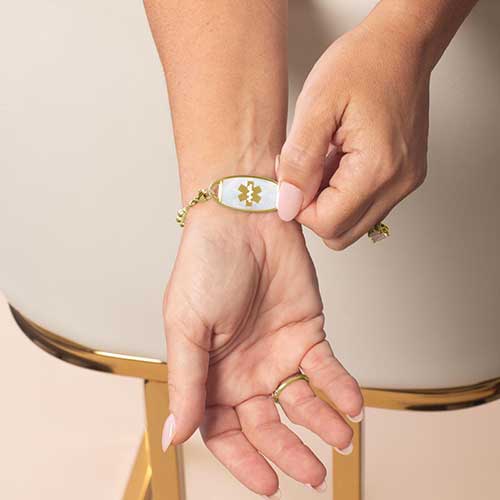 Model is wearing a gold-tone medical ID bracelet with a mother-of-pearl inlay tag featuring the Star of Life symbol.