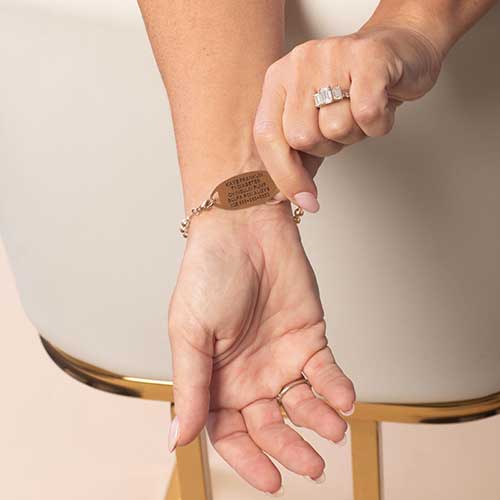 Model is wearing a rose gold-tone medical ID bracelet, displaying the back of the ID tag with personalized medical engraving.