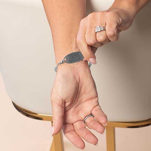 Model is wearing a silver-tone medical ID bracelet, displaying the back of the ID tag with personalized medical engraving.
