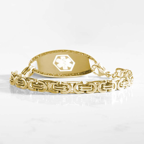 Gold-tone medical ID bracelet with interlocking links and a polished tag, shown at a low angle on a white surface.