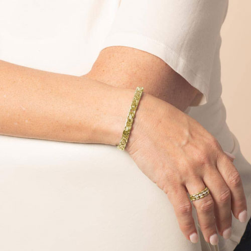 Model wearing a gold-tone Beckett medical ID bracelet with rectangular patterned links, shown on the wrist with a gold-tone ring.
