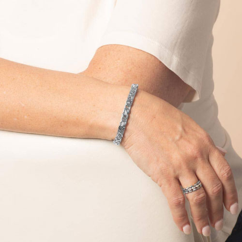 Model wearing a silver-tone Beckett medical ID bracelet with rectangular patterned links, shown on the wrist with a silver-tone ring.