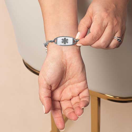 Woman showing decorative medical alert tag with red medical caduceus symbol*