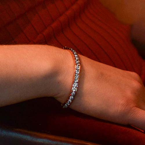 Woman in orange dress wearing 12k gold plated medical ID tennis bracelet with clear cubic zirconia crystals.