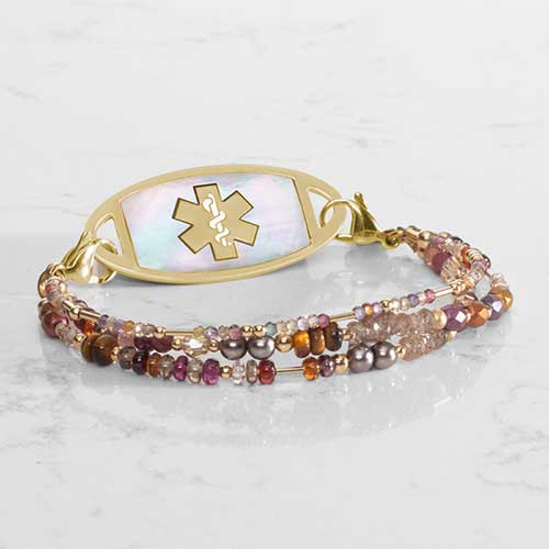 Fawn Medi ID bracelet paired with gold and mother of pearlr inlaid med ID tag on white marble countertop.