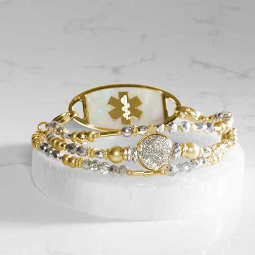 Three-strand beaded medical ID bracelet in silver and gold tones, displayed flat with engraved tag showing.