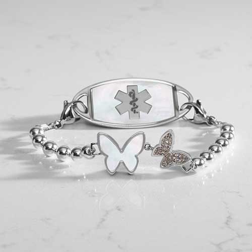 Serenity Stretch Bracelet with silver beads, featuring a double butterly centerpiece with crystals and mother of pearl inlay, attached to a silver medical ID tag with mother of pearl inlay and silver caduceus.