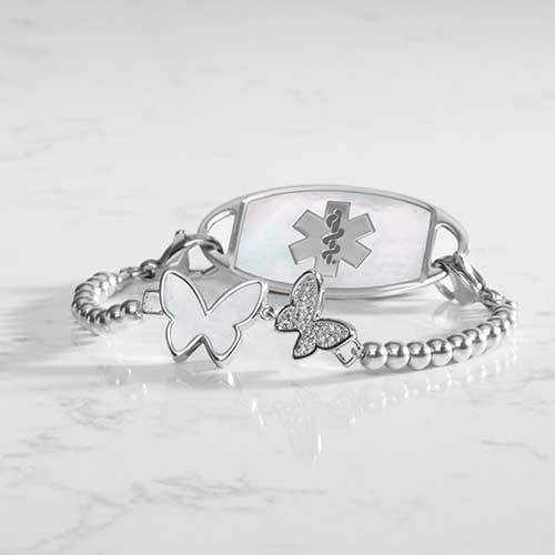 Serenity Stretch Bracelet with silver beads, featuring a double butterly centerpiece with crystals and mother of pearl inlay, attached to a silver medical ID tag with mother of pearl inlay and silver caduceus.