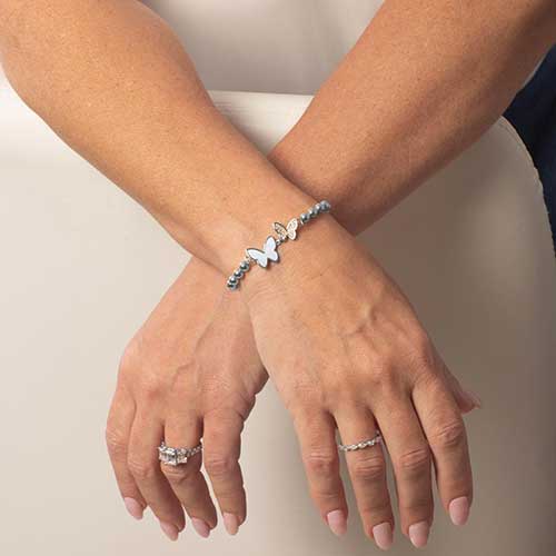 Woman wearing silver beaded stretch bracelet with double butterfly centerpiece featuring crystals and mother of pearl inlay.